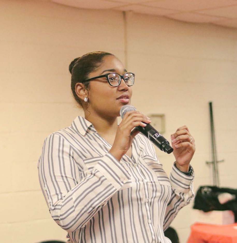 A woman in glasses is speaking into a microphone.