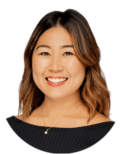 A woman with shoulder-length wavy hair smiles, wearing a black top and a gold necklace with a pendant.