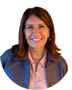 A smiling woman with shoulder-length brown hair, wearing a light pink collared shirt under a gray jacket.
