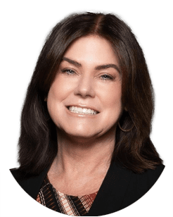 Woman with medium-length dark brown hair, wearing a black blazer and patterned top, smiling at the camera against a plain light background.