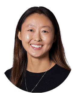 A woman with long, straight hair smiles at the camera. She is wearing a black top and a necklace.