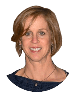 A woman with short, light brown hair, smiling, wearing earrings and a necklace, and dressed in a dark top.