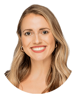 A woman with long blonde hair smiles at the camera, wearing hoop earrings and a light top.