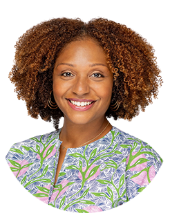A smiling woman with afro hair in a floral shirt.