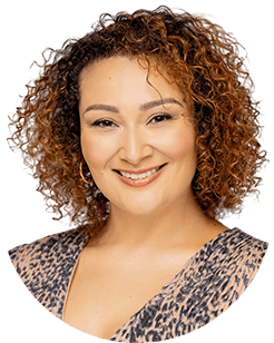 A woman with curly hair smiling in a leopard print top.