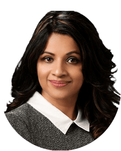 A woman with dark, wavy hair wearing a grey sweater with a white collar, smiling at the camera.