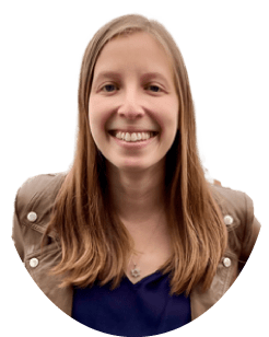 A woman with long light brown hair and a smile, wearing a brown jacket over a dark top.