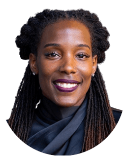 A person with long braided hair and wearing a dark outfit, smiling.