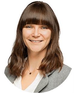 Person with long brown hair and fringe, smiling, wearing a white shirt and gray blazer.