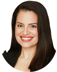 A woman with long dark hair is smiling. She is wearing a black top and has light skin.