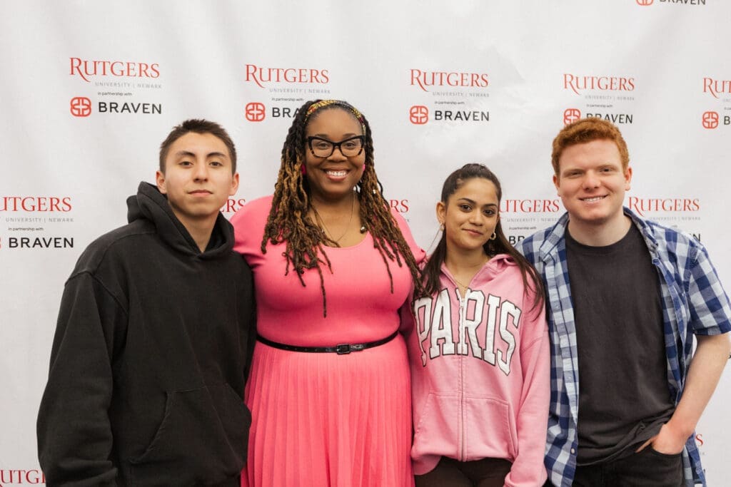 Four individuals stand together in front of a Rutgers University and Braven backdrop.