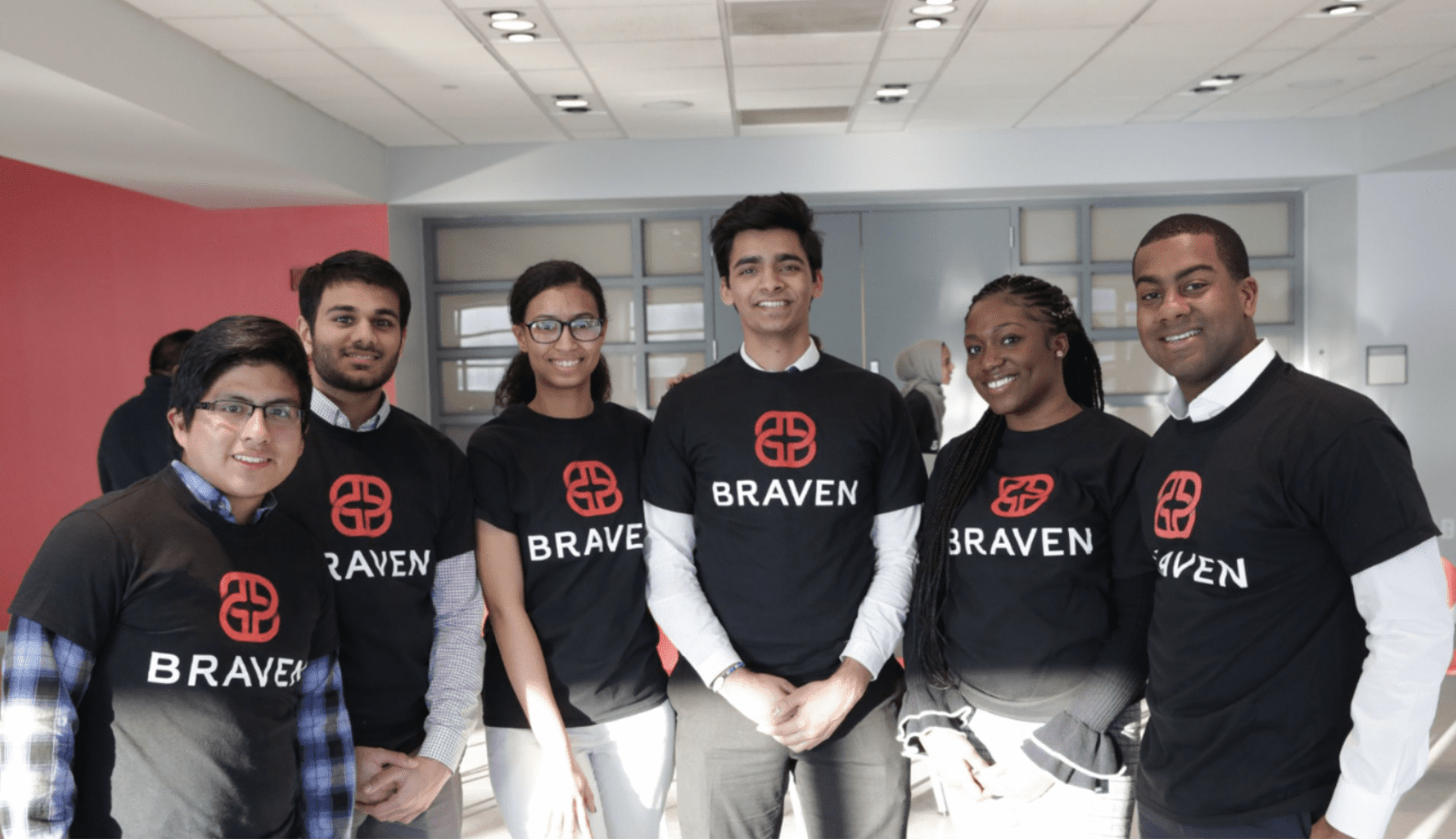 A group of six people wearing matching "Braven" shirts stands together in a brightly lit room.