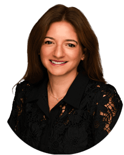 Woman with long brown hair wearing a black lace top, smiling at the camera against a plain light background.