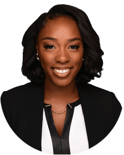 Portrait of a woman with short, styled black hair, wearing a black blazer over a white blouse with a black trim, smiling at the camera against a plain background.