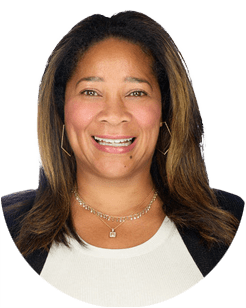 Smiling person with long hair wearing a black blazer and white top against a plain background.