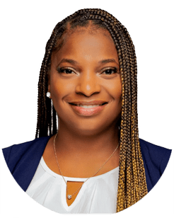 Person smiling, wearing a blue blazer, white top, and necklace. Hair styled in long braids. White background.