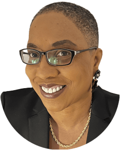 A person wearing glasses, a black blazer, gold necklace, and earrings, smiling at the camera against a white background.