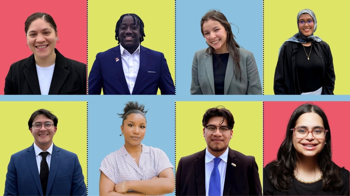 Group portrait of eight professionally dressed individuals, each shown from the waist up, against color-blocked yellow, pink, and blue backgrounds.
