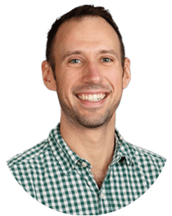 A man with short brown hair and light skin smiles at the camera. He is wearing a green and white checkered shirt. The background is white.