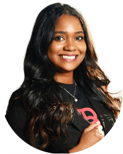 Smiling woman with long wavy hair wearing a black blazer and a black shirt, posing in front of a plain light background.