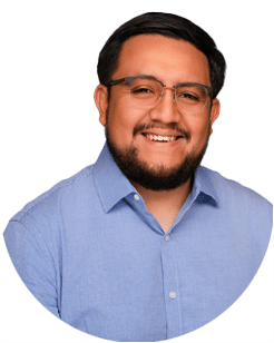 Man with short black hair, glasses, and a beard, wearing a light blue button-up shirt, smiling at the camera against a plain background.