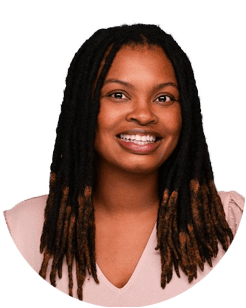 Smiling woman with long, dark, and light brown dreadlocks wearing a light pink top, posed against a plain white background.