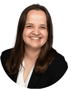 A woman with long brown hair, wearing a black blazer and white shirt, smiles at the camera against a plain light background.
