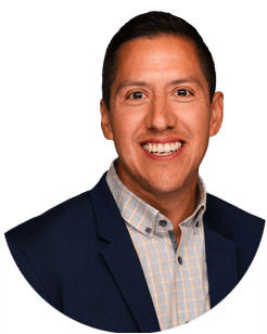 Smiling man with short dark hair wearing a blue blazer and a light-colored checked shirt, posed against a plain white background.