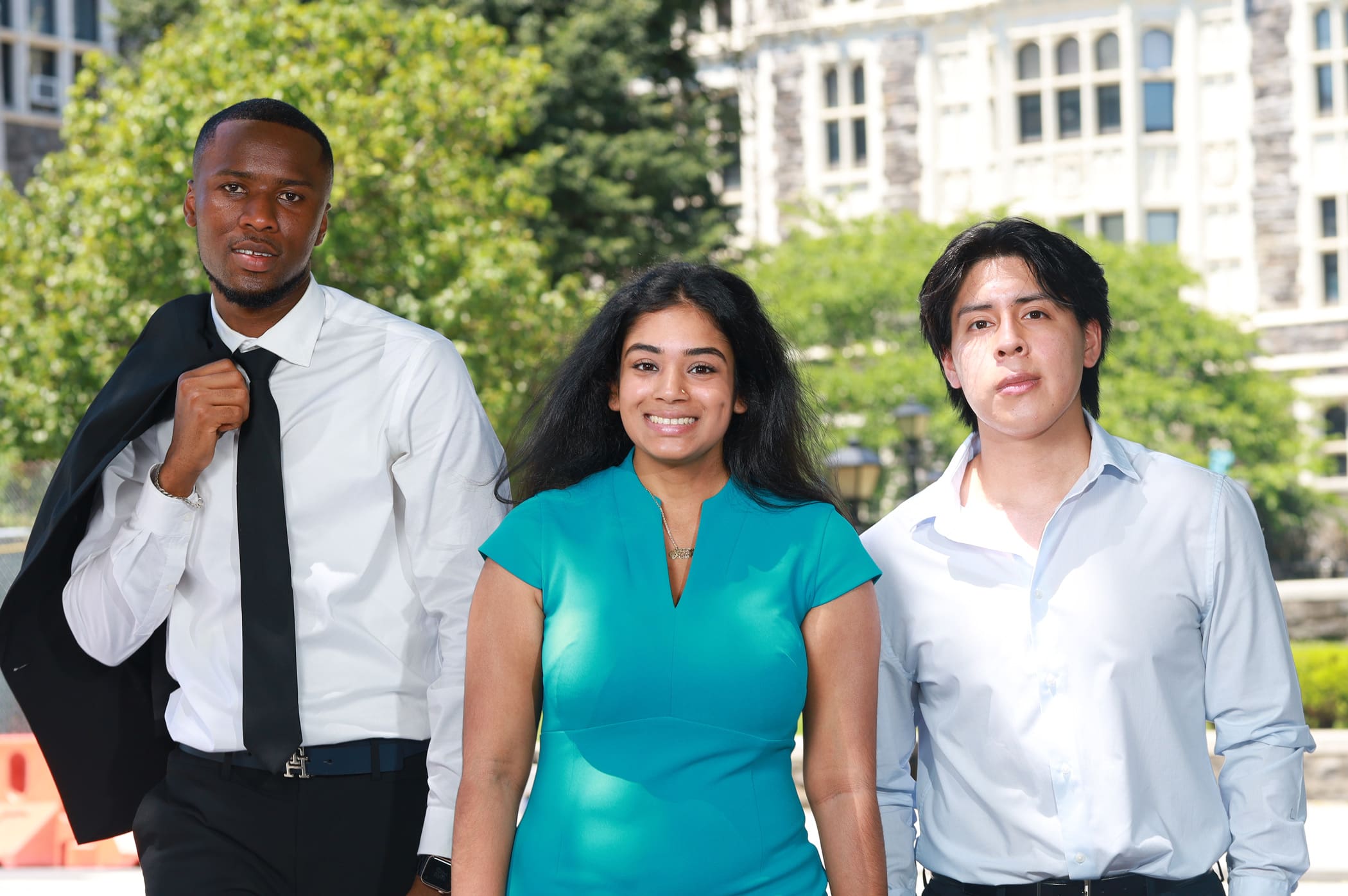 Three people stand outdoors in business attire, with trees and a building in the background, looking directly at the camera.