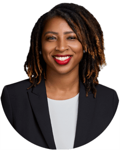 A woman with shoulder-length locs, wearing a black blazer and white top, smiles at the camera against a plain background.