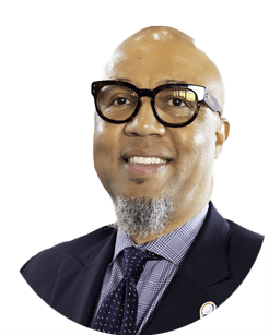 A bald man with glasses, a goatee, and a suit smiles at the camera against a plain white background.
