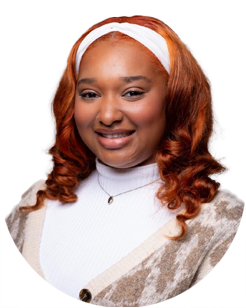 Woman with long, curly red hair wearing a white headband, white turtleneck, necklace, and patterned cardigan, smiling at the camera against a plain background.