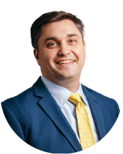 Man in a blue suit, white shirt, and yellow tie, smiling at the camera against a plain light background.