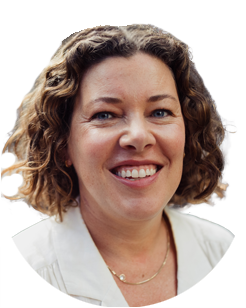 Woman with curly brown hair smiling, wearing a white top and a thin necklace, against a plain light background.