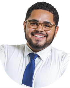 A man with short curly hair, beard, and glasses, wearing a white shirt and blue tie, smiling at the camera against a plain background.