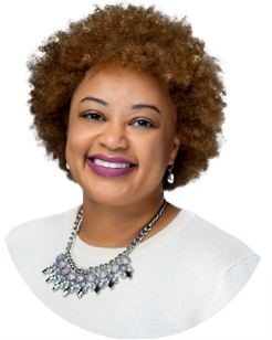 A woman with curly brown hair, wearing a white top, a statement necklace, pearl earrings, and pink lipstick, smiling at the camera.