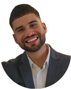 Man with short dark hair and beard, wearing a gray suit jacket and white shirt, smiling at the camera against a plain background.