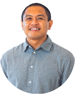 A man with short hair smiles at the camera, wearing a light blue button-up shirt against a plain light background.