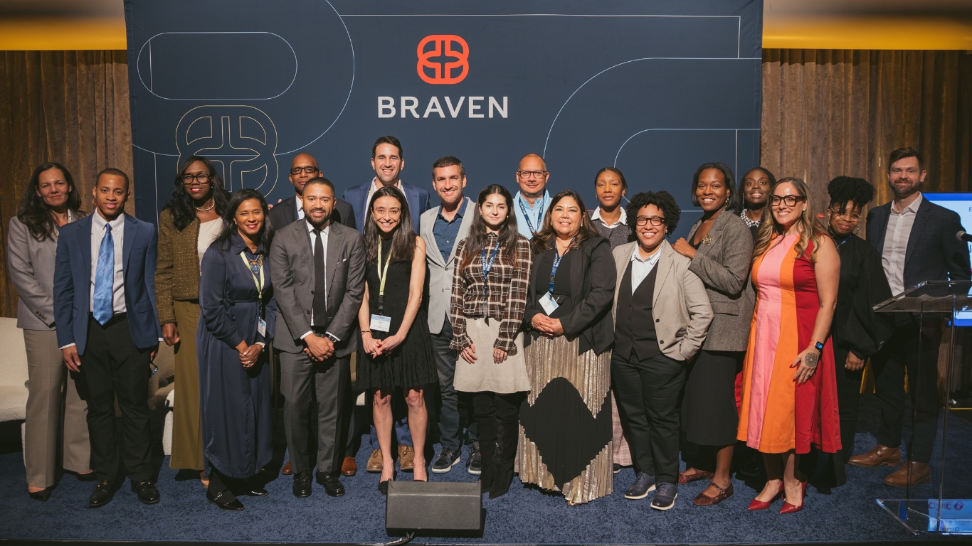 A large group of people standing in a row in front of a blue Braven company backdrop.